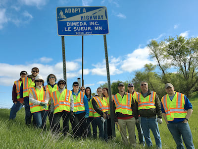 group of lesueur employees standing in front of adopt a highway sign